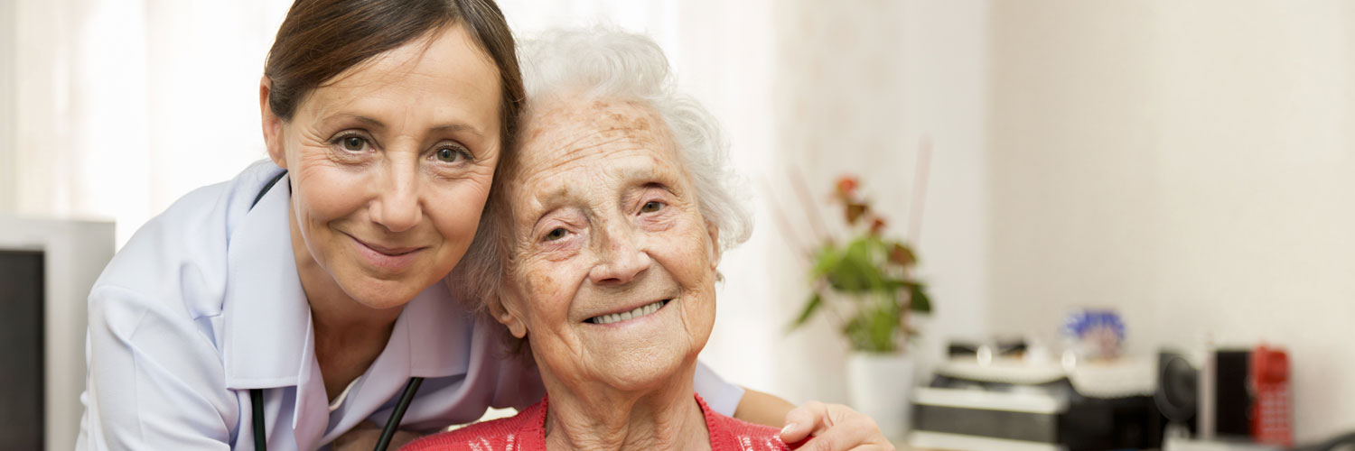 caregiver and elderly woman hugging and smiling at the camera